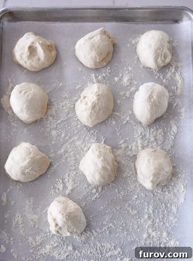 Ten uniformly shaped sourdough flatbread dough balls resting on a lightly floured, parchment-lined baking sheet.