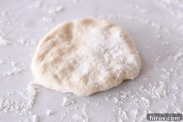 A thin circle of sourdough flatbread dough on a lightly floured counter.