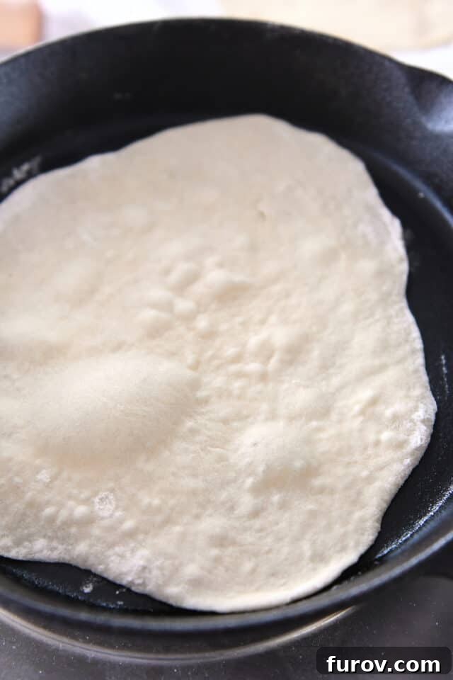 A sourdough flatbread bubbling and cooking in a hot cast iron skillet.