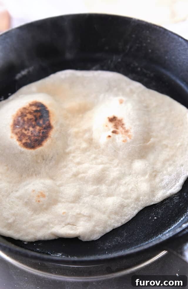 Another sourdough flatbread cooking in a cast iron skillet, showing a golden underside.