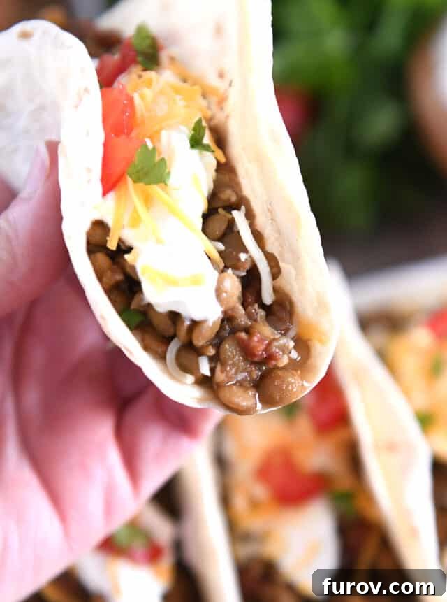 One-Pot Wonder Lentil Tacos 8 Holding flour tortilla with cooked lentils, sour cream, cheese and tomatoes.