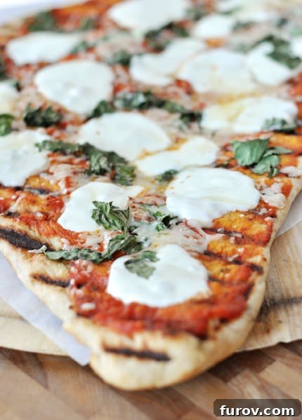 A perfectly grilled pizza with fresh mozzarella melted on top, garnished with green herbs, ready to be sliced.