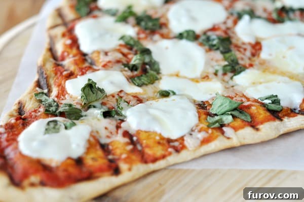 A triangle-shaped grilled pizza slice with vibrant red sauce, perfectly melted fresh mozzarella circles, and a sprinkle of fresh herbs.