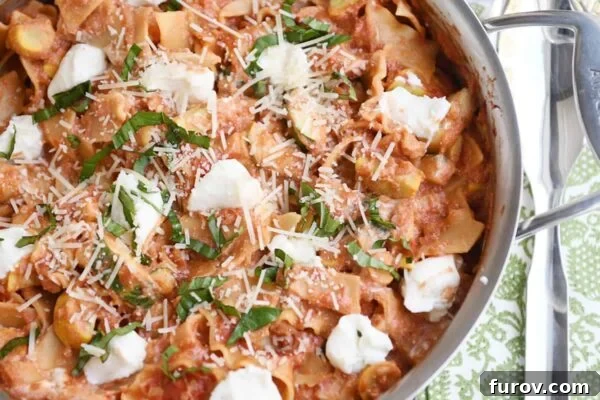 Close-up view of Skillet Vegetable Lasagna simmering in a stainless steel pan, with visible noodles and vegetables, topped with dollops of ricotta.