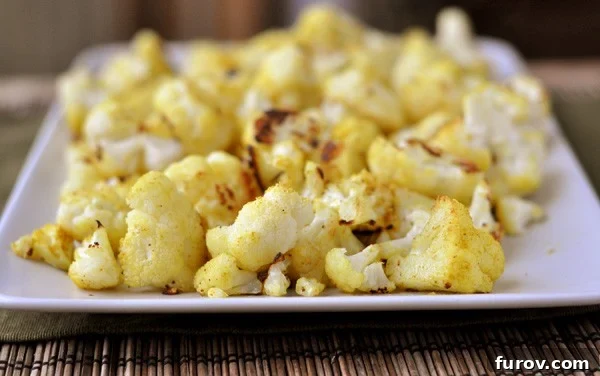A side view of a white platter with cooked cauliflower florets, showcasing their golden-brown color and appealing texture.