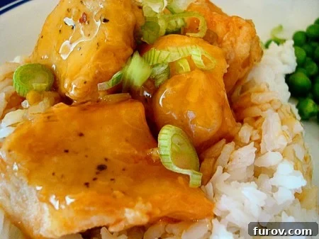 Delicious baked orange chicken served on a bed of fluffy white rice, garnished with green onions.