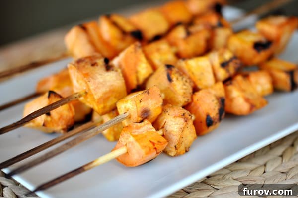 Rectangular white platter showcasing perfectly grilled sweet potato skewers, garnished lightly.