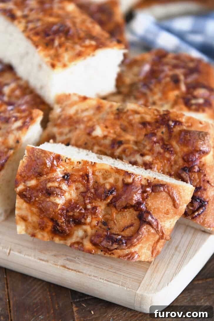 Three golden-brown slices of Italian cheese bread topped with melted cheese and herbs, resting on a rustic wood cutting board.