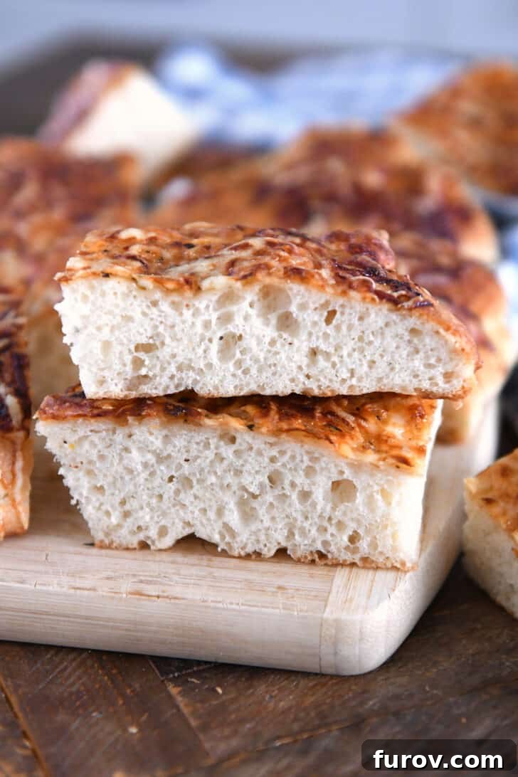 Two fluffy, golden-crusted slices of Italian cheese bread, perfectly stacked on a wooden cutting board, showcasing the soft interior and melted cheese.