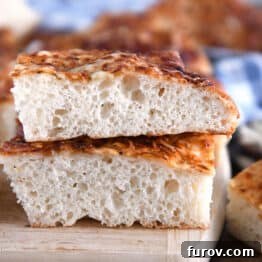 Two stacked pieces of fluffy Italian cheese bread on wood cutting board.