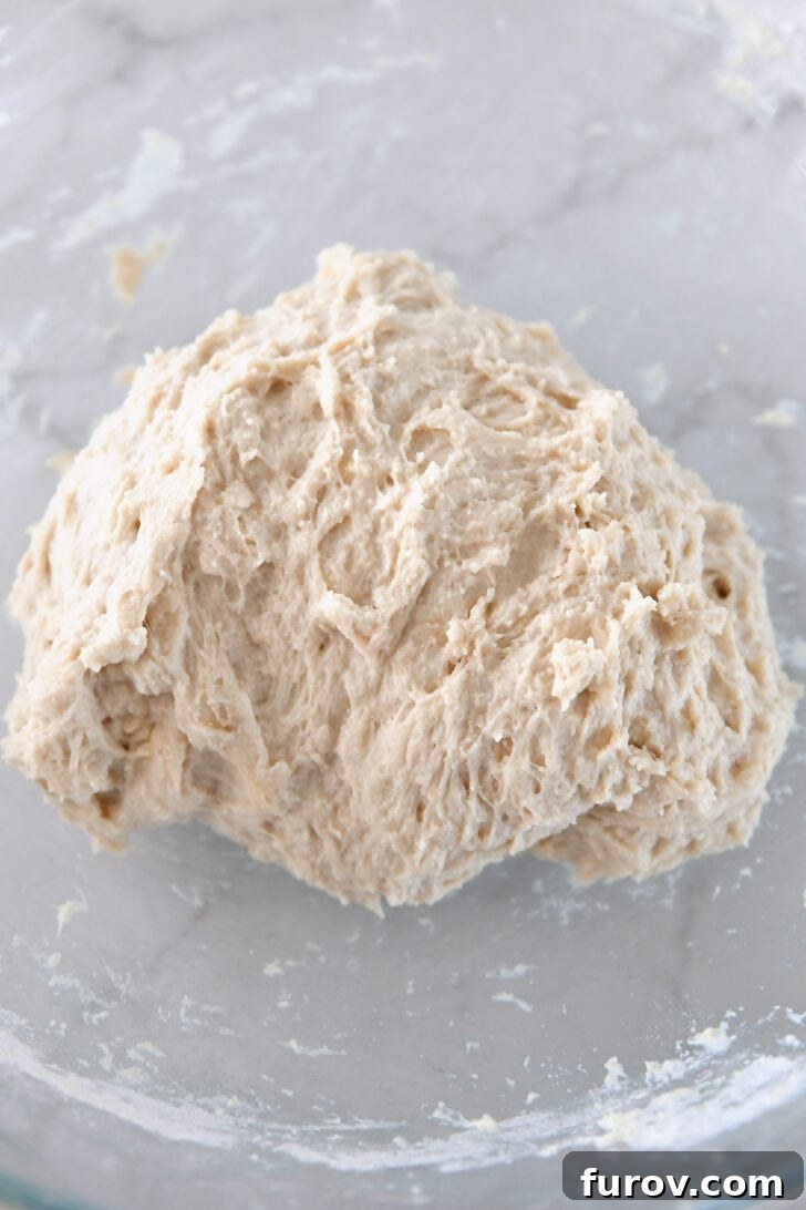 Hand-mixed bread dough in a glass bowl, shaped into a rough ball, ready for its first rise.