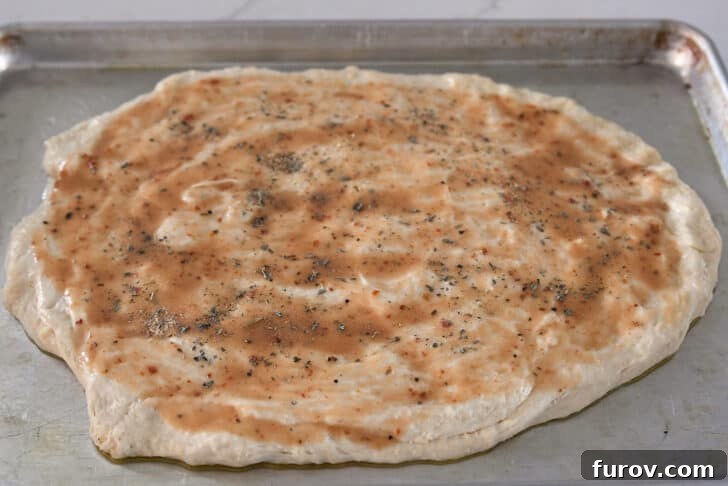 A mixture of dried Italian herbs and salt being sprinkled uniformly over the salad dressing-brushed bread dough.