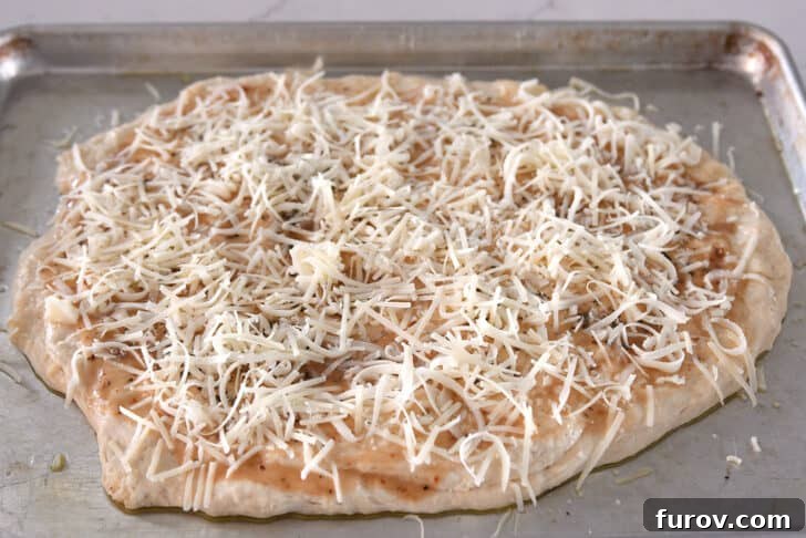 Generous layers of shredded mozzarella and freshly grated Parmesan cheese covering the seasoned bread dough, ready for baking.