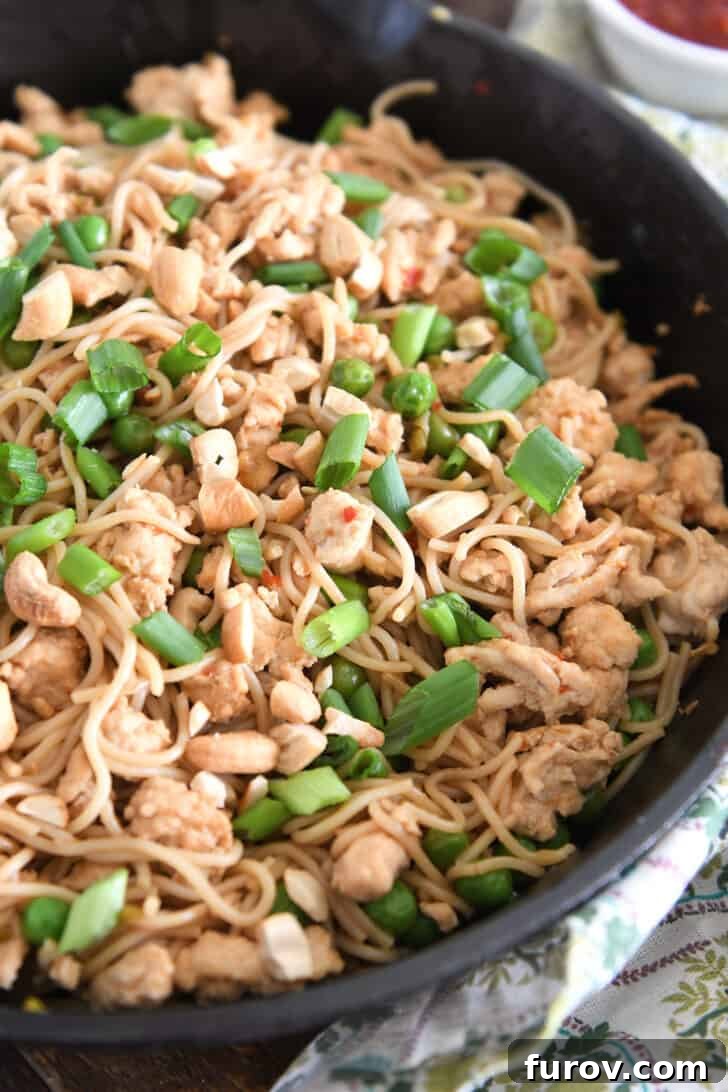 A vibrant bowl of spicy garlic ramen noodles, garnished with peas, ground turkey, and fresh green onions, invitingly presented in a rustic cast iron skillet.