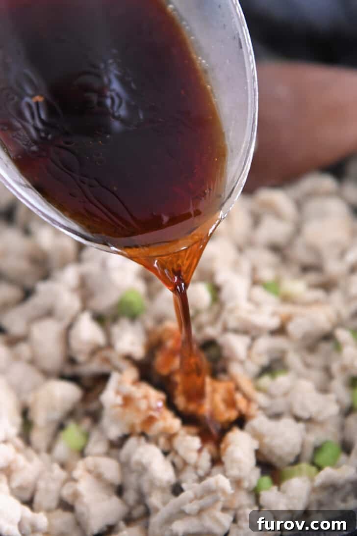 A cook pouring the vibrant spicy garlic sauce into a hot skillet, where seasoned ground turkey is cooking, setting the stage for flavor infusion.