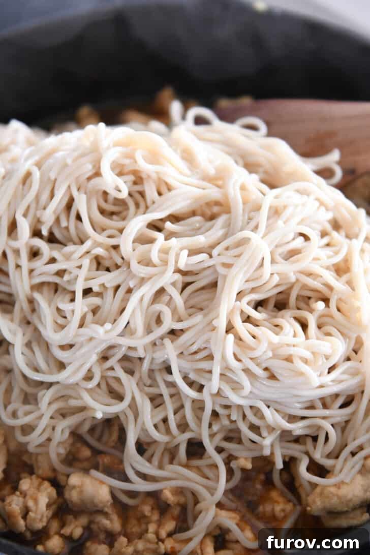 Freshly cooked ramen noodles added to a skillet containing perfectly browned ground turkey, ready to be tossed with the delicious sauce.