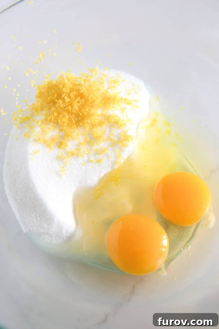Glass bowl with granulated sugar, lemon zest, and eggs.