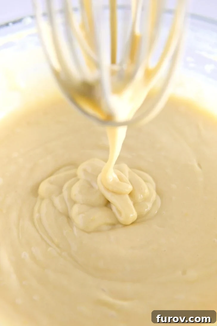 Whisk drizzling olive oil cake batter into glass bowl.