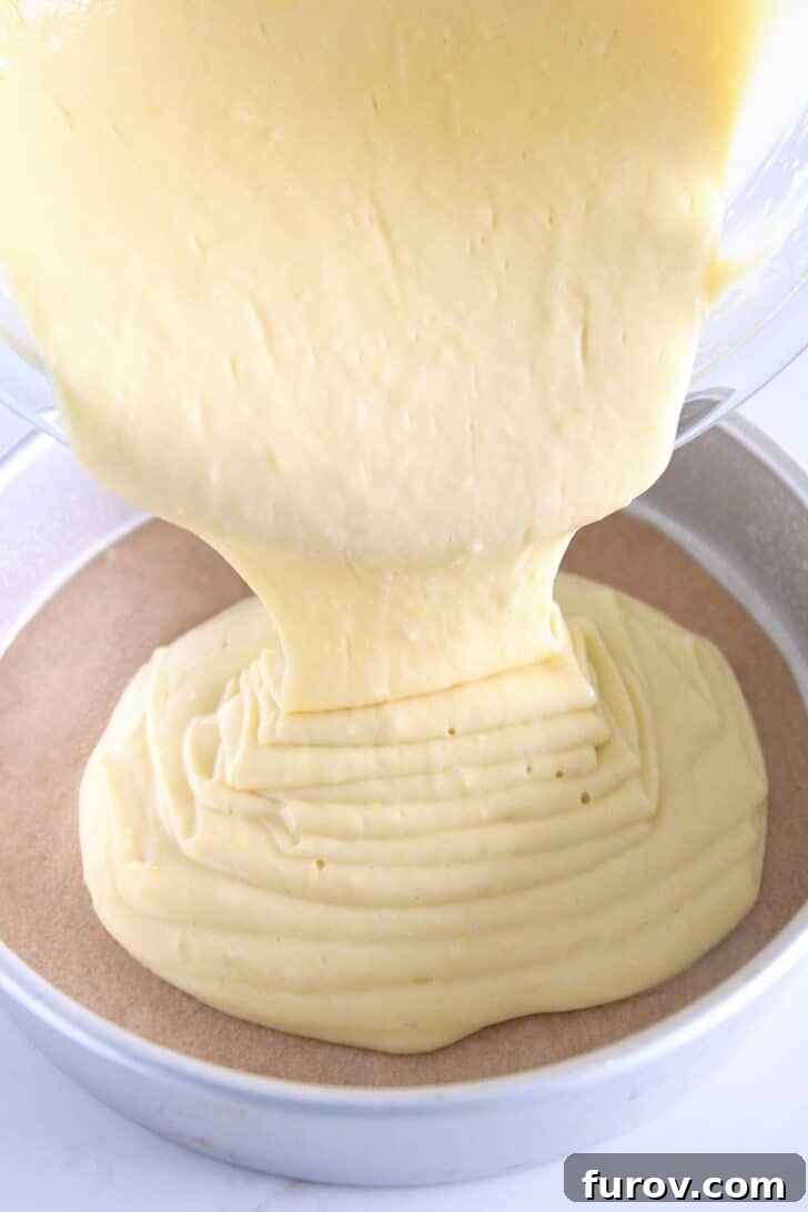 Pouring olive oil cake batter into parchment paper-lined round baking pan.