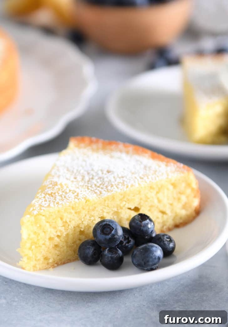 Triangle of olive oil cake dusted with powdered sugar on white plate with blueberries.