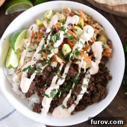 White bowl with rice, Korean beef, slaw, sauce, and lime wedges, a perfect Korean Beef Bowl.