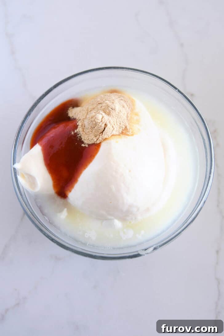Small glass bowl containing sour cream, mayonnaise, garlic powder, and sriracha, key ingredients for the creamy spicy sauce.
