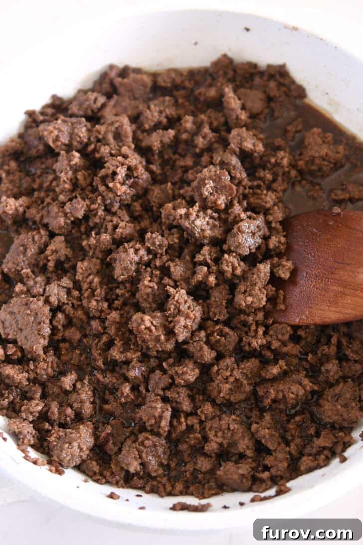 White skillet with perfectly browned Korean-style ground beef and a wooden spoon, ready to be seasoned.