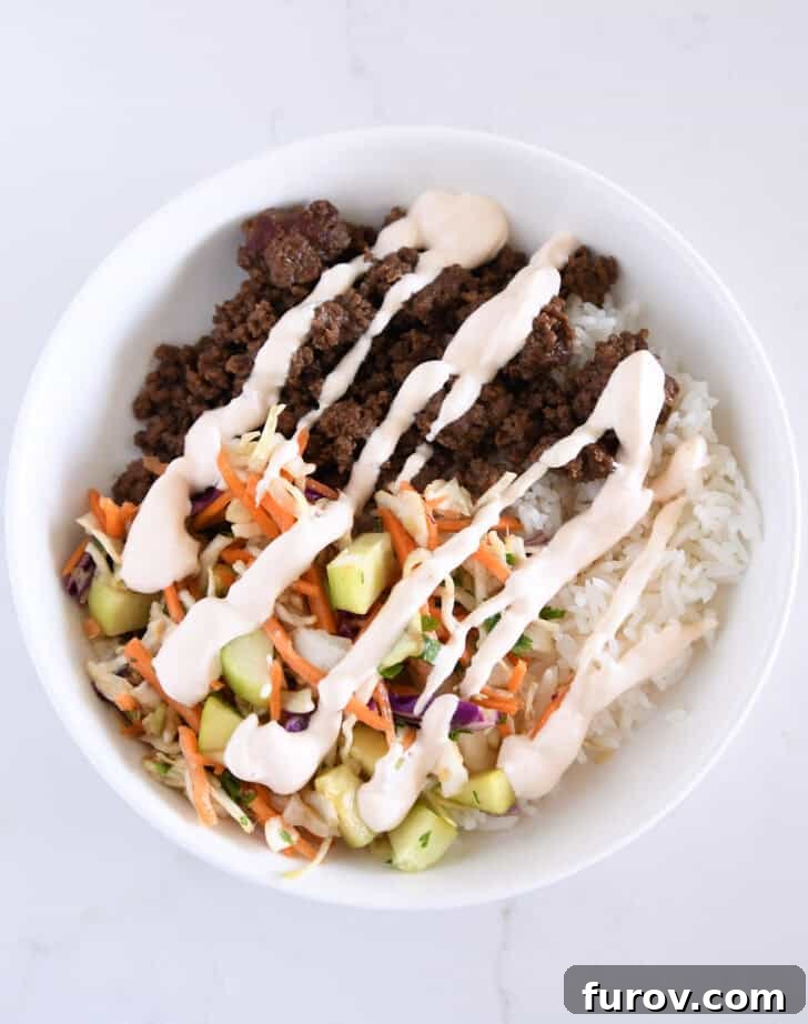 White bowl with rice, refreshing slaw, crisp cucumbers, and savory ground beef, showcasing a nearly complete bowl.