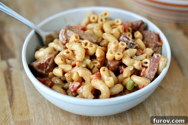 A vibrant white bowl of BBQ Macaroni Salad, showcasing tender elbow noodles, diced turkey kielbasa, and colorful vegetables, all coated in a rich, creamy sauce, ready to be served.