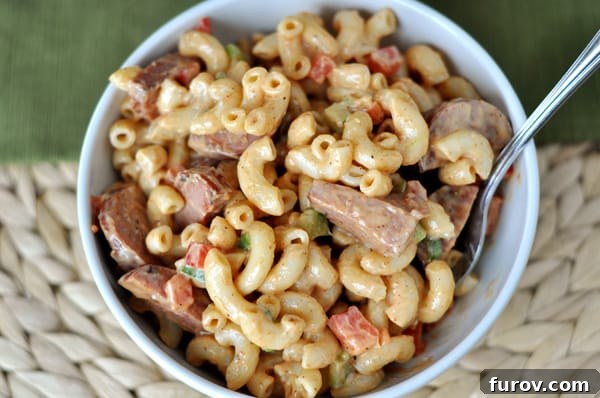 An overhead shot of a generous serving of BBQ Macaroni Salad in a white bowl, highlighting the texture of the elbow noodles, finely diced ham, and vibrant green onions mixed throughout the creamy, flavorful dressing.