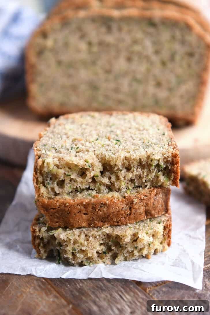 Three half slices of zucchini bread loaf stacked neatly on white parchment paper, showcasing its moist interior and golden-brown crust. A perfect display of this ultimate quick bread.