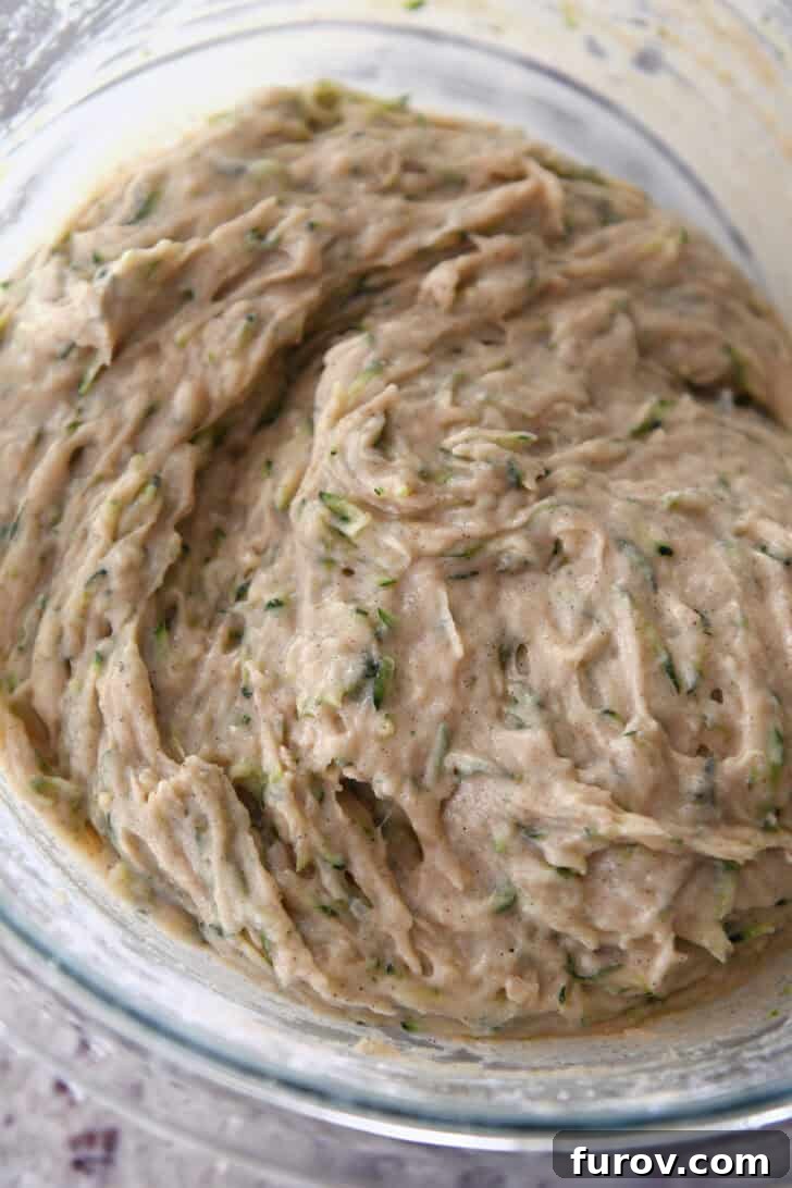 A glass bowl showcasing the perfectly mixed zucchini bread batter, appearing smooth yet with a desirable slight lumpiness, indicating it has not been overmixed.