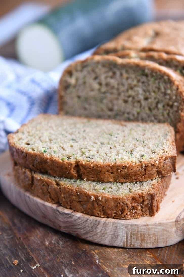 Two perfectly cut slices of zucchini bread, showcasing the soft, moist interior flecked with green zucchini, resting on a rustic wooden cutting board.