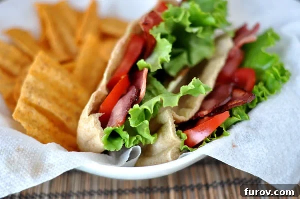 A beautifully presented, cut-open BLT pita pocket showcasing the layers of turkey bacon, lettuce, tomato, and avocado spread, served alongside a handful of crispy chips in a rustic white paper-lined basket.