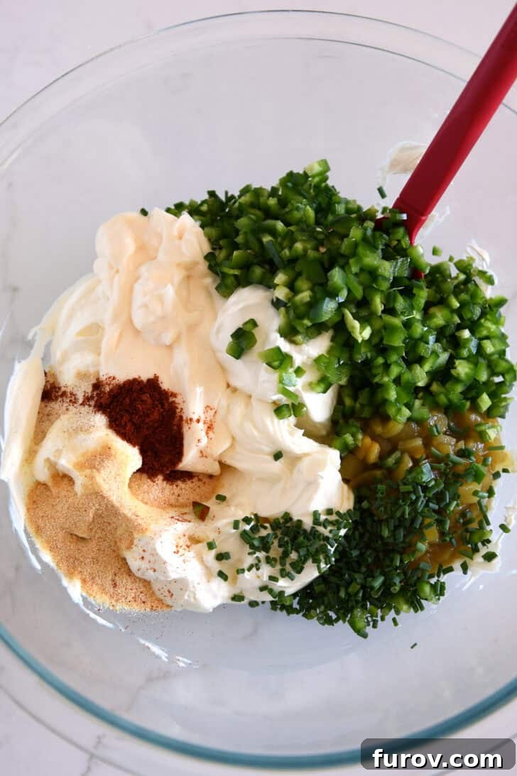 Glass bowl with sour cream, mayo, green onions, chopped jalapenos, green chiles and spices.