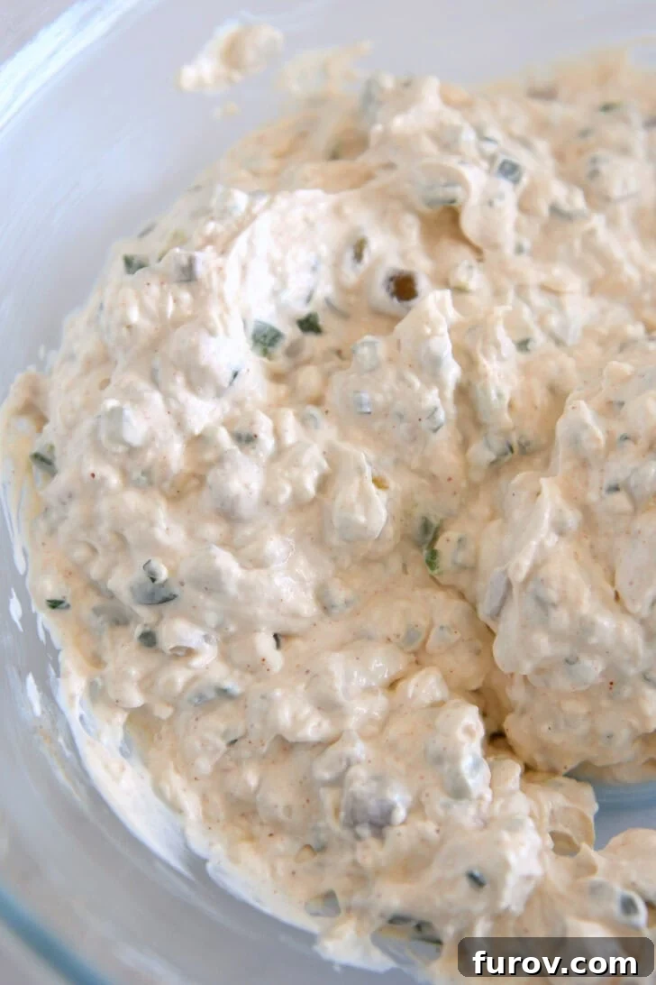Glass bowl with creamy mixture of jalapenos, mayo, sour cream, green onions.