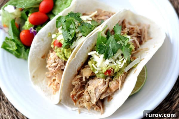 Top view of two soft shell tacos filled with juicy Cuban pork, red onion, and cilantro on a white plate, ready to be eaten.