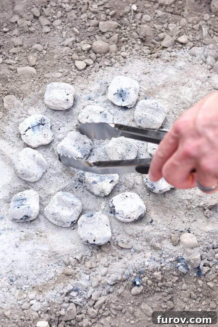 Ultimate Dutch Oven Lasagna 13 Hot coals being carefully placed in a circular pattern on the dirt, ready for a Dutch oven.