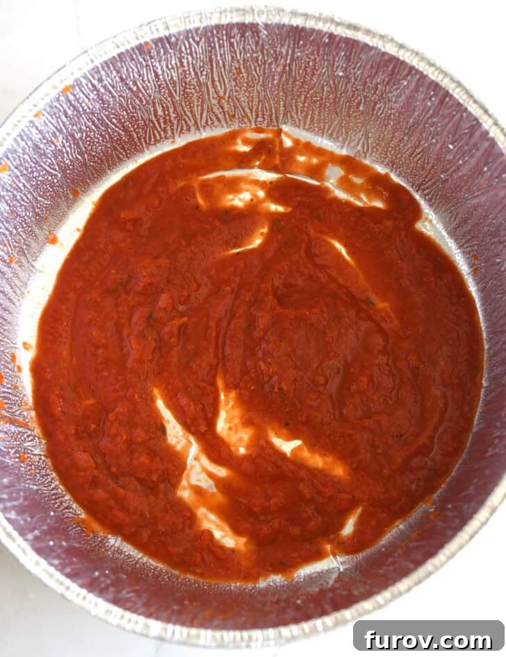 Ultimate Dutch Oven Lasagna 5 Top-down view of a Dutch oven liner with a layer of pasta sauce spread on the bottom.