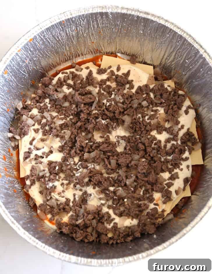 Ultimate Dutch Oven Lasagna 8 Top-down view of ground beef and cooked onions layered over the creamy mixture in the Dutch oven liner.