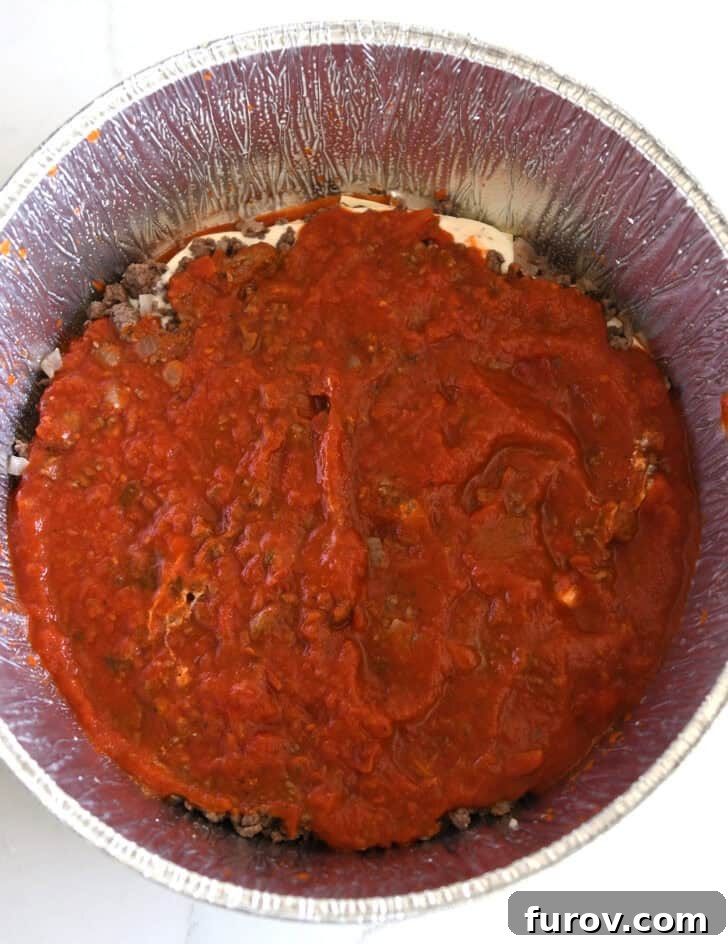 Ultimate Dutch Oven Lasagna 9 Top-down view of a layer of pasta sauce generously poured over the meat mixture in the Dutch oven liner.