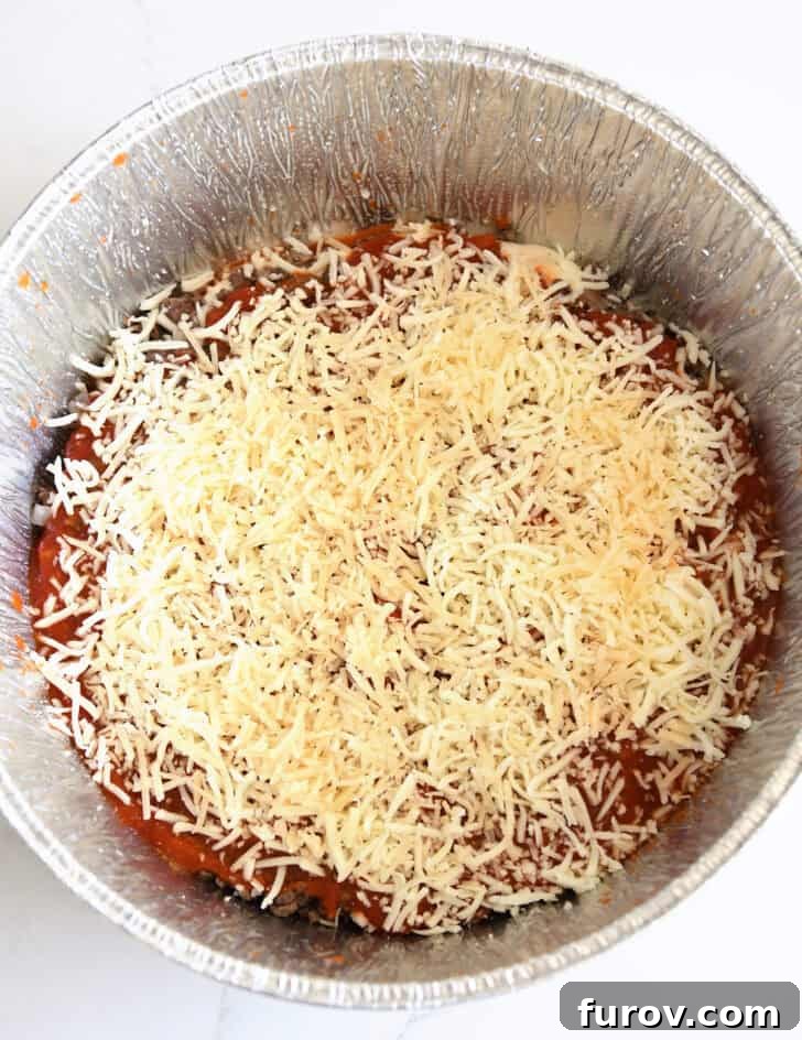 Ultimate Dutch Oven Lasagna 10 Top-down view of a generous layer of shredded cheese topping the lasagna in the Dutch oven liner.