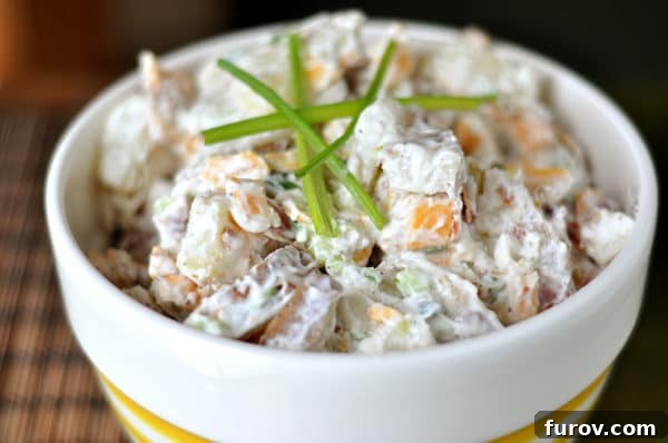 White bowl full of baked potato salad with sprigs of chives on top, ready to be served as a delightful summer side dish.