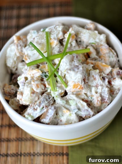 Top view of a white bowl full of baked potato salad with stalks of chives on top, emphasizing its creamy texture and vibrant garnishes.