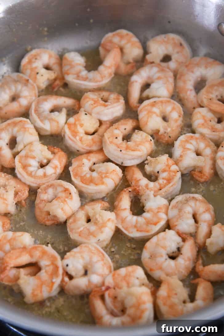 Garlic Butter Shrimp and Sausage Skillet 4 Fresh shrimp cooking in fragrant garlic butter within a gleaming stainless steel pan.