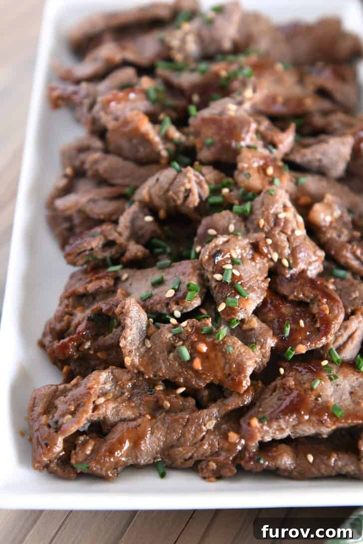 A white tray generously piled with perfectly cooked, thinly sliced beef bulgogi, garnished with fresh green onions and toasted sesame seeds, ready to serve.