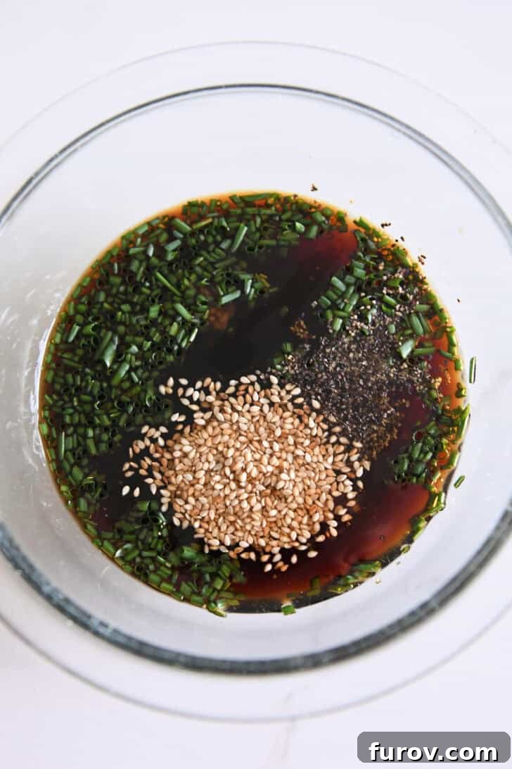 Top-down view of a glass bowl filled with the bulgogi marinade, showcasing soy sauce, toasted sesame seeds, freshly ground pepper, and vibrant green onions.