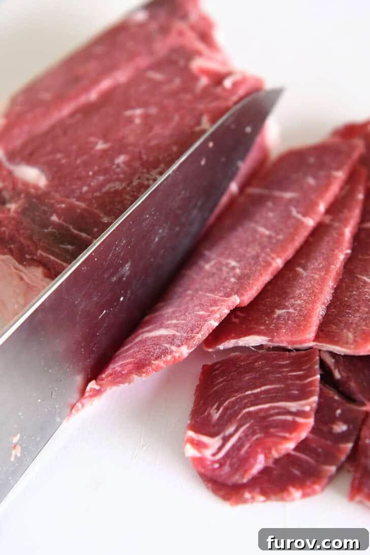 Close-up shot of thinly sliced beef pieces on a white cutting board next to a sharp knife, illustrating the precise preparation needed for bulgogi.