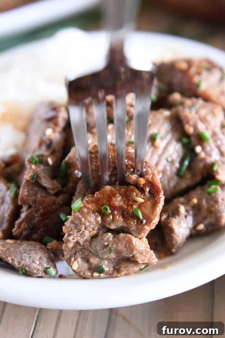 A fork delicately piercing a piece of perfectly cooked beef bulgogi, highlighting its tenderness and inviting texture.
