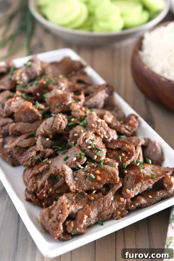 A white tray brimming with beautifully cooked beef bulgogi, generously drizzled with a rich Korean sauce and garnished with fresh green onions and toasted sesame seeds, ready for serving.